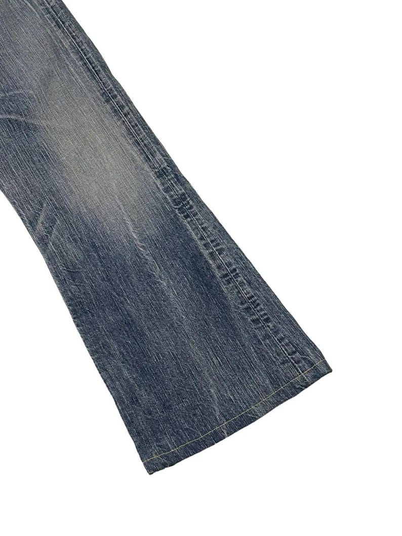 May include: Close-up of a section of blue denim jeans. The jeans have a faded wash and visible stitching along the seams. The fabric appears worn, with subtle variations in color.