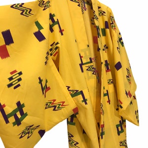 May include: A yellow kimono with a geometric pattern in shades of purple, green, red, and orange. The kimono is hanging on a hanger.