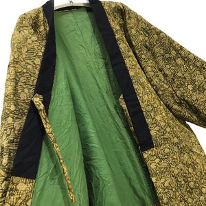 May include: A green and gold patterned kimono with black trim. The kimono is open and the lining is visible. The lining is a solid green color.