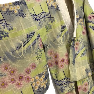 May include: A green and blue patterned kimono with a white collar. The kimono has a floral design with pink and white flowers.