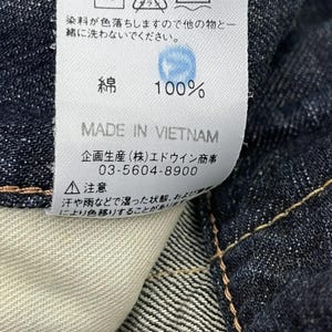 Puede incluir: Primer plano de una etiqueta blanca con texto japon&eacute;s y s&iacute;mbolos de cuidado, adherida a una tela vaquera azul oscuro. La etiqueta indica que la tela es 100% algod&oacute;n y est&aacute; hecha en Vietnam. Tambi&eacute;n se incluyen instrucciones de lavado.