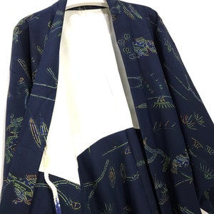 Könnte beinhalten: Ein marineblauer Kimono mit weißem Futter und einem bunten Blumenmuster. Der Kimono hat einen langen, fließenden Ärmel und einen breiten Kragen.