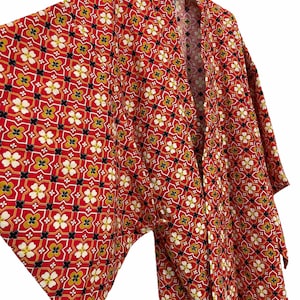 Könnte beinhalten: Ein roter Kimono mit einem geometrischen Muster aus weißen, gelben und schwarzen Blumen. Der Kimono hat einen langen Ärmel und einen weiten Kragen.
