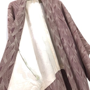 Könnte beinhalten: Ein mauvefarbenes Kimono mit einem weißen geometrischen Muster. Das Kimono ist geöffnet, um ein weißes Futter zu zeigen. Das Kimono hängt an einem Kleiderbügel mit dem aufgedruckten Wort "AKAGAMI".