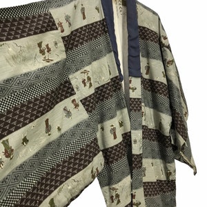 May include: A traditional Japanese kimono with a patchwork design featuring various patterns and figures. The kimono is made of a light-colored fabric with brown and green accents. The fabric has a subtle sheen and a soft texture.