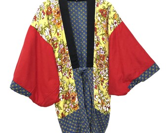 May include: A yellow, red, and blue patterned kimono with a black collar and tie. The kimono has a floral print and is hanging on a hanger.