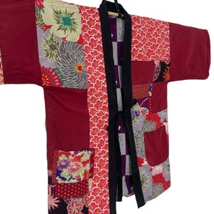 May include: A patchwork kimono in shades of red, burgundy, and floral patterns. The kimono features a black tie closure and pockets. The design incorporates various floral and geometric patterns.