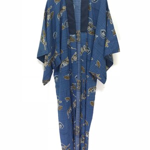 May include: Blue kimono with a geometric pattern and Japanese-style illustrations. The kimono has a dark blue collar and is hanging on a wooden hanger. The fabric is a light blue with a grid pattern and brown and white illustrations.
