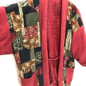 Könnte beinhalten: Ein roter Kimono mit einem geometrischen Muster in Braun-, Grün- und Schwarztönen. Der Kimono hat einen Bindegürtel und zwei Taschen.