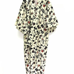 Könnte beinhalten: Ein cremefarbener Kimono mit einem schwarzen und roten Blumenmuster. Der Kimono hat lange Ärmel und einen V-Ausschnitt.