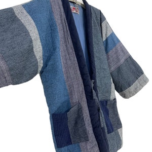 May include: A blue and white striped quilted kimono with a navy blue collar and tie. The kimono has two pockets on the front.
