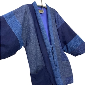 May include: A blue and indigo patchwork kimono with a tie closure and two pockets. The kimono has a label that reads "Made in Japan".