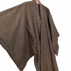 May include: A brown striped Japanese kimono with a long sleeve and a sash. The kimono is hanging on a hanger.
