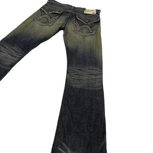 Puede incluir: Vaqueros de mezclilla azul descolorido con dise&ntilde;o de pierna acampanada. Los vaqueros presentan costuras detalladas, bolsillos traseros decorativos y una peque&ntilde;a etiqueta roja. La mezclilla tiene un aspecto desgastado.