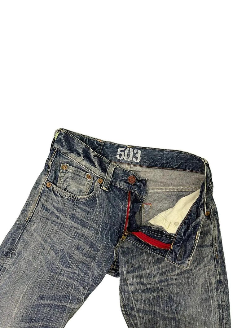May include: Blue denim jeans with a distressed wash and a red zipper. The jeans have the number "503" printed on the waistband. The jeans are unbuttoned and unzipped, showing the interior.