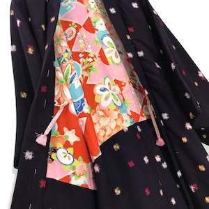 May include: A dark purple kimono with a white and pink geometric pattern. The kimono is open to reveal a colourful floral lining.