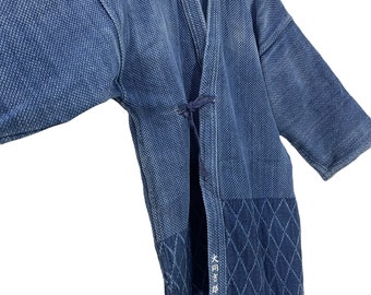 May include: A blue cotton Japanese  "Jinbei"  robe with a diamond pattern on the bottom. The robe has a tie closure and is hanging on a hanger. The text "日本製" is embroidered on the robe, which translates to "Made in Japan".