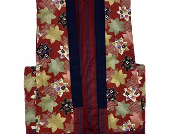 May include: A red and black patterned vest with a navy blue collar and trim. The vest has a floral design and is quilted. The vest is hanging on a hanger with a tag that says "AKASAMI".
