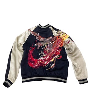 May include: A black bomber jacket with a large embroidered dragon design on the back. The dragon is depicted in shades of red, orange, and yellow, with a detailed, multi-colored design. The sleeves are a cream color, and the jacket has black and white striped cuffs.