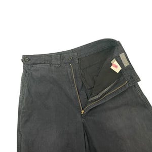 Puede incluir: Pantalones grises oscuros con cremallera y cierre de botón visibles. Los pantalones tienen un diseño clásico con corte recto. La tela parece ser un material duradero, adecuado para el uso diario. Los pantalones se muestran sobre un fondo blanco.