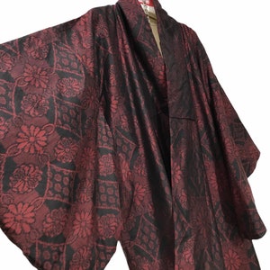 May include: A burgundy kimono with a floral pattern in black. The kimono is hanging from a chain and has wide sleeves. The fabric has a sheen, and the floral design is visible throughout the garment.