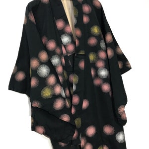 May include: A black kimono with a pattern of pink, white, and gold circles. The kimono is hanging on a hanger with a red tag that says "AKAGAMI".
