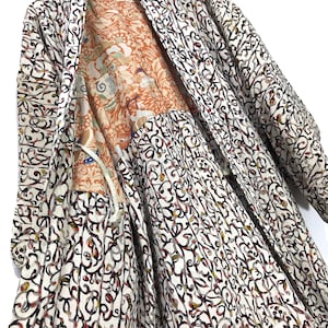 Puede incluir: Un kimono blanco con un estampado floral negro y rojo. El kimono está abierto para revelar un forro floral colorido.