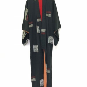 May include: A black kimono with a geometric pattern in shades of gray, red, and white. The kimono has a long, flowing silhouette and a wide, open collar. The fabric is soft and silky.