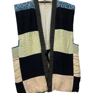May include: A patchwork vest with a blue, black, white, and beige color scheme. The vest has a traditional Japanese design with a floral pattern and a tie closure.
