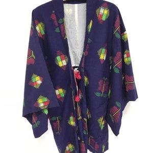 May include: A dark blue kimono with a colorful geometric pattern. The kimono has a tie at the front and tassels on the ends of the tie.
