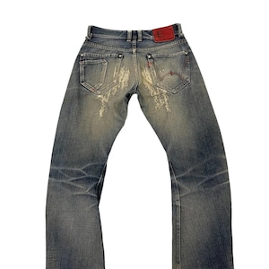 Puede incluir: Vaqueros de mezclilla azul descolorido con detalles desgastados. Incluye un parche de cuero rojo con una "E" blanca en la parte trasera y un dise&ntilde;o cosido en rojo en el bolsillo trasero. Los vaqueros tienen un dise&ntilde;o cl&aacute;sico de cinco bolsillos.