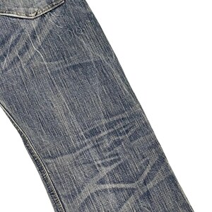 May include: Close-up of blue denim jeans with a faded, worn appearance. The jeans have a classic five-pocket design, with a visible back pocket and detailed stitching. The fabric shows signs of wear and tear, adding to the vintage aesthetic.