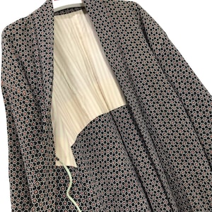 Könnte beinhalten: Ein Kimono mit schwarzem und weißem Muster und einem roten geometrischen Design. Der Kimono hängt an einem Kleiderbügel mit einem roten Etikett, auf dem "AKAGAMI" steht.