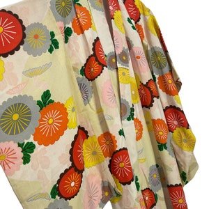 May include: A cream-coloured kimono with a floral pattern. The flowers are red, orange, yellow, green, and grey. The kimono is made of a lightweight fabric and has a traditional Japanese design.