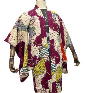 Puede incluir: Un kimono japonés vintage con un fondo morado vibrante y un patrón floral y geométrico colorido. El kimono tiene mangas largas y un cuello ancho.