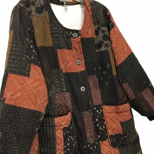 May include: A long-sleeved patchwork jacket with a brown, orange, and black color scheme. The jacket has a button closure and two large pockets. The fabric has a quilted texture.