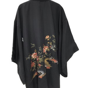 May include: A black silk kimono with a floral design. The flowers are pink, red, and white, and the leaves are green. The kimono is hanging on a hanger.