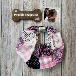 May include: A circular pet collar accessory featuring a patchwork design of pink and white gingham, black and white polka dots, and floral patterns in shades of pink, white, and navy blue. The fabric is gathered with an elasticized band.