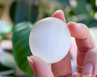 May include: A white selenite sphere, a smooth, polished crystal ball, held in a hand.