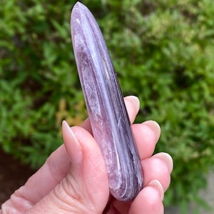 May include: A polished purple and white striped crystal wand. The wand is smooth and has a rounded tip.