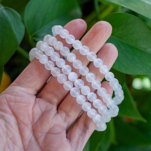 May include: Three white beaded bracelets stacked on top of each other. The bracelets are made of smooth, round beads.