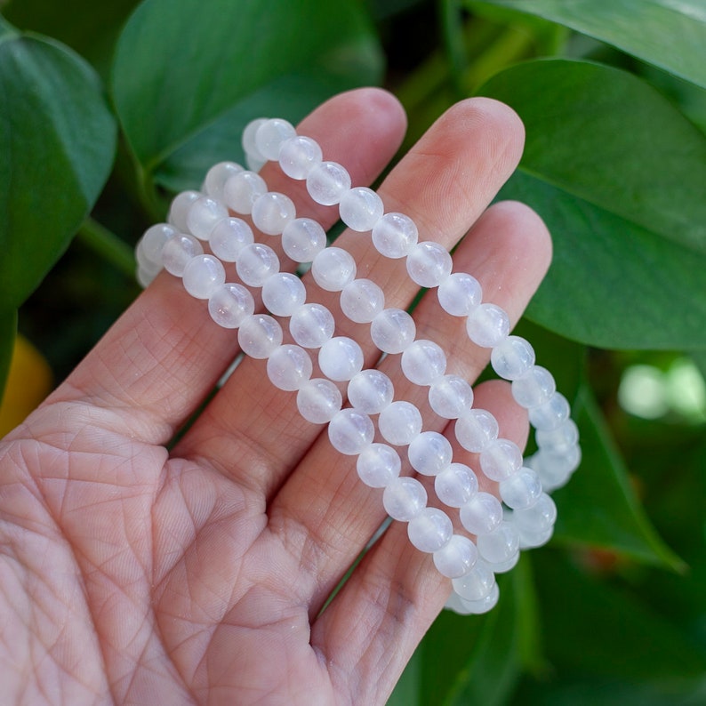 May include: Three white beaded bracelets stacked on top of each other. The bracelets are made of smooth, round beads.