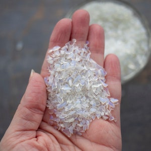 May include: A handful of iridescent white opal chips. The chips are small and irregular in shape, with a pearly sheen.