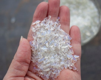 May include: A handful of iridescent white opal chips. The chips are small and irregular in shape, with a pearly sheen.