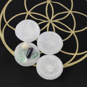 May include: Four clear, round stones are arranged on a black surface with a gold geometric design. One stone contains smaller, colorful stones. The image suggests a spiritual or metaphysical theme.