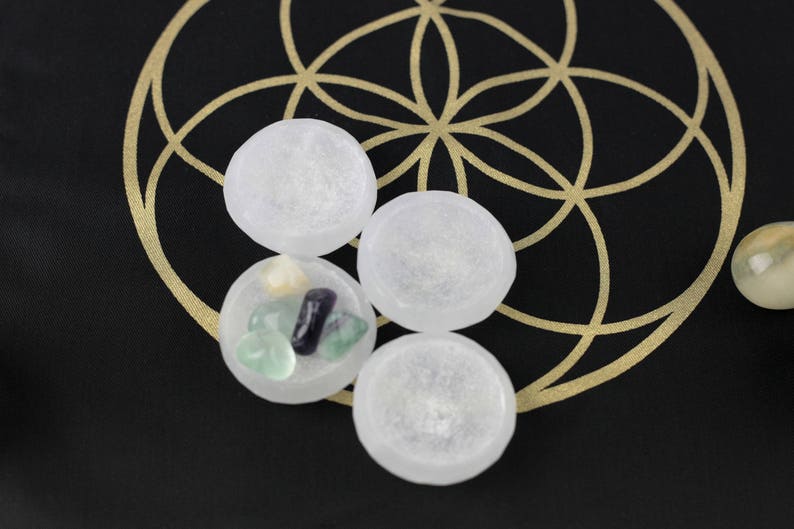 May include: Four clear, round stones are arranged on a black surface with a gold geometric design. One stone contains smaller, colorful stones. The image suggests a spiritual or metaphysical theme.