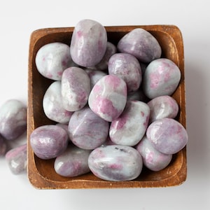May include: A bowl of tumbled pink and white lepidolite stones. The stones are smooth and polished, with a variety of shapes and sizes.