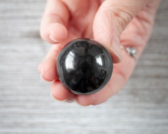May include: A smooth, black obsidian sphere, polished to a high shine, held in a hand.