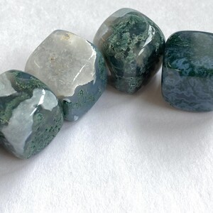 Puede incluir: Cuatro piedras de &aacute;gata musgosa pulidas con bordes redondeados. Las piedras muestran una mezcla de colores blanco transl&uacute;cido, azul y verde. Las inclusiones verdes se asemejan a musgo o patrones vegetales. Las piedras est&aacute;n dispuestas sobre una superficie blanca.