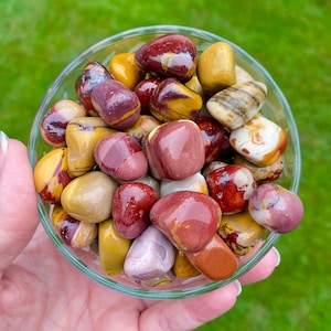 May include: A bowl of colorful tumbled stones, including red, brown, yellow, and white. The stones are smooth and polished, and they have a variety of patterns and textures.